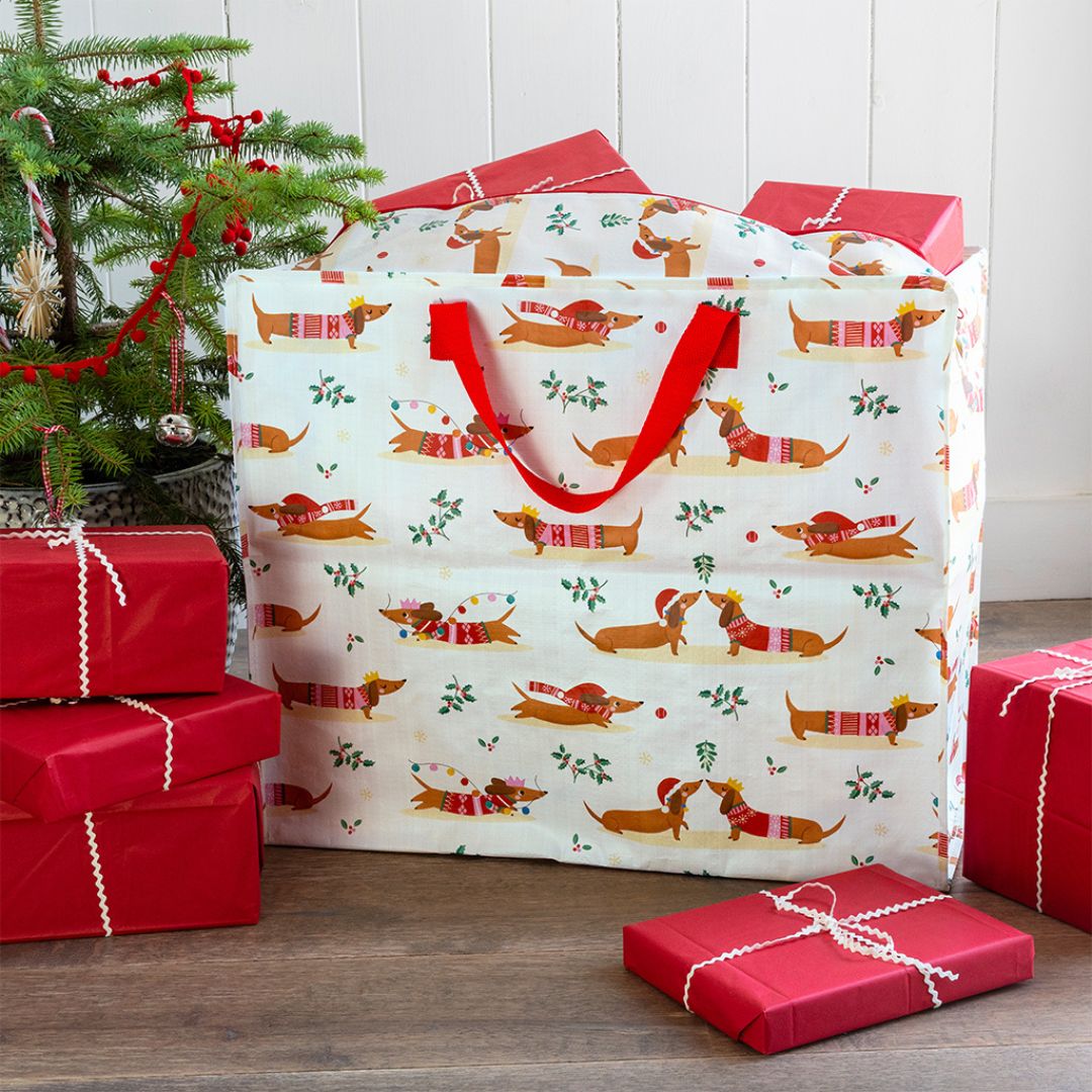 Rex London jumbo opbergtas met kerst worsthondjes patroon, gevuld met cadeaus naast een kerstboom.