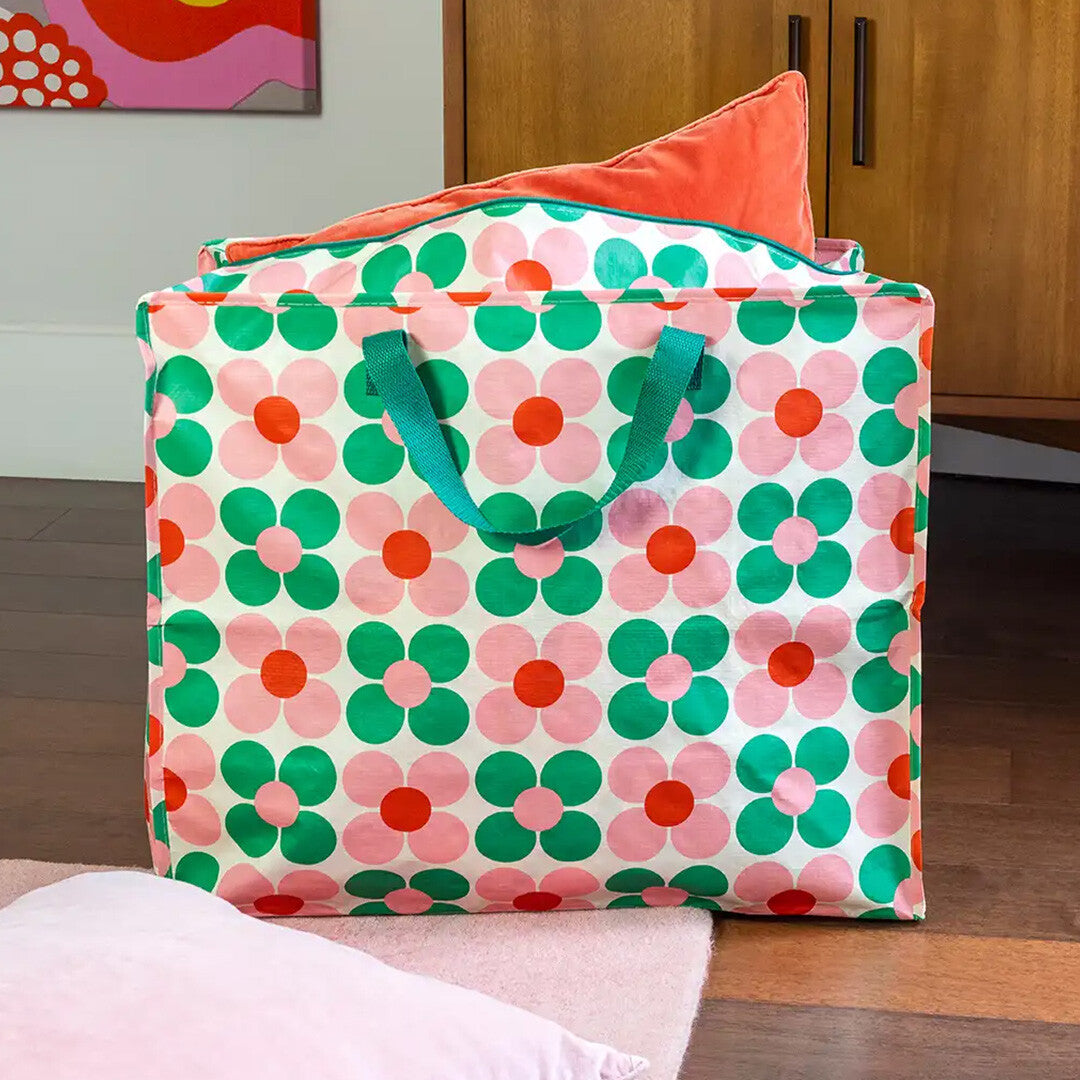 Rex London jumbo opbergtas met roze en groen margrietpatroon, gevuld met een oranje kussen, staand op een vloerkleed.
