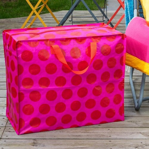Rex London jumbo opbergtas met rode stippen op roze, staand op een houten vlonder.
