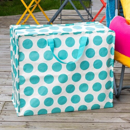 Rex London jumbo opbergtas met turquoise stippen op een houten terras, naast kleurrijke meubels.