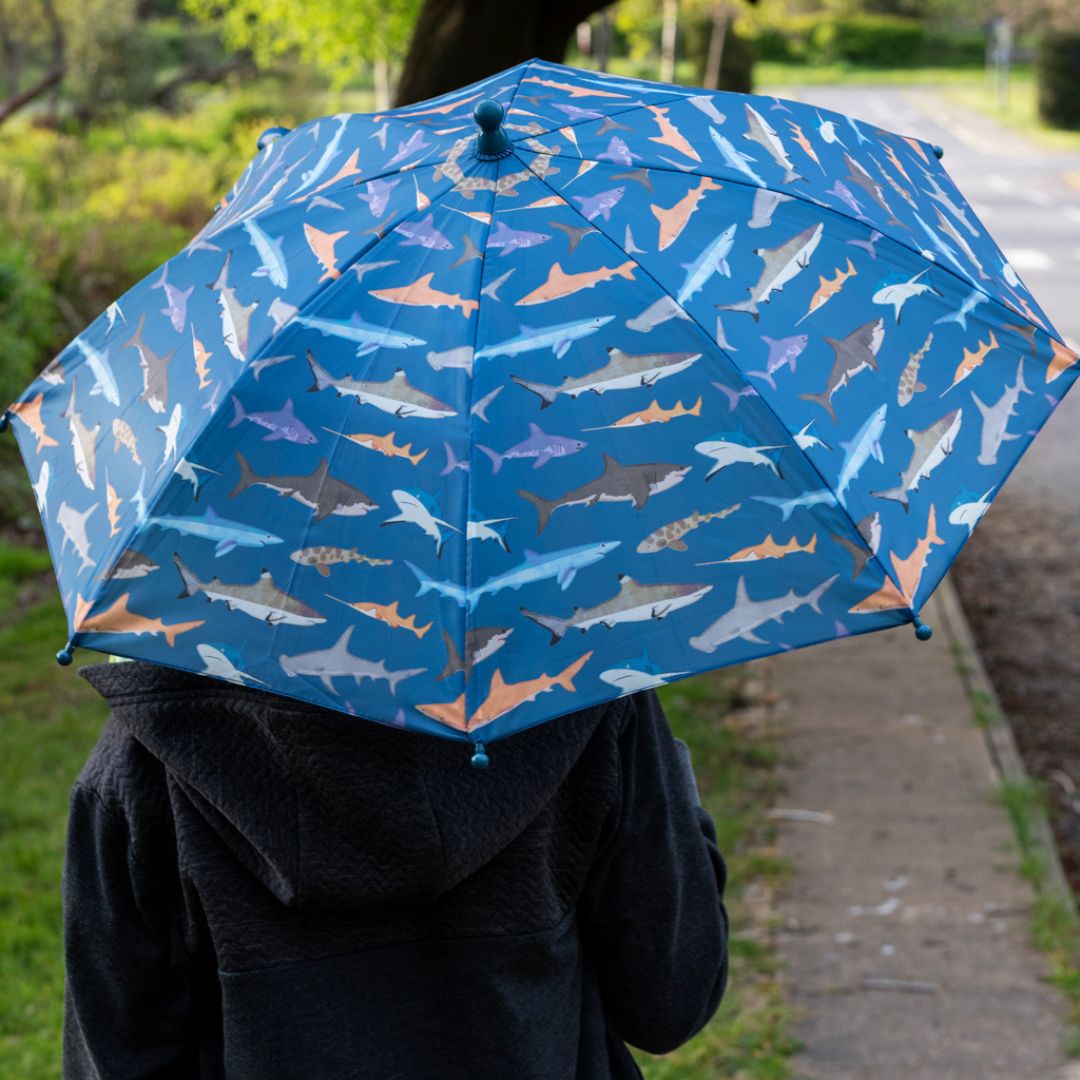 Kind van achteren gezien met een open Rex London kinderparaplu met haaienpatroon.