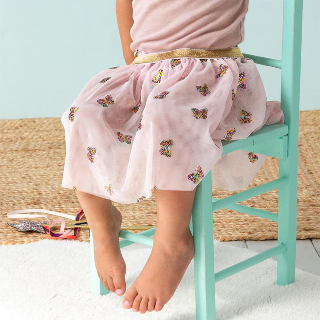 De roze kinderrok met vlinderpailletten gedragen door een kind dat op een groene stoel zit.