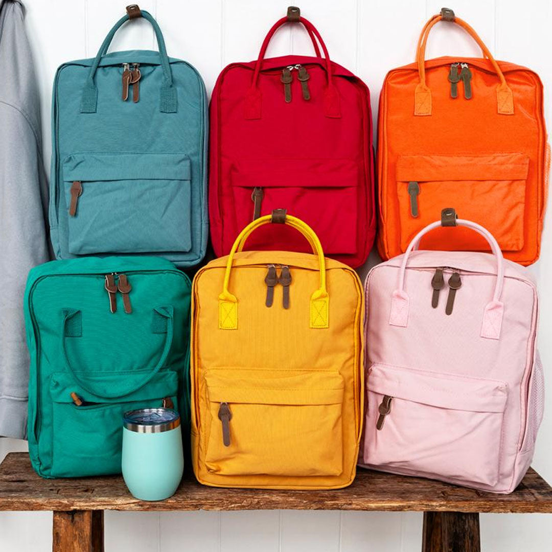 Collectie Rex London compacte kinderrugzakken in zes verschillende kleuren op een houten bank.
