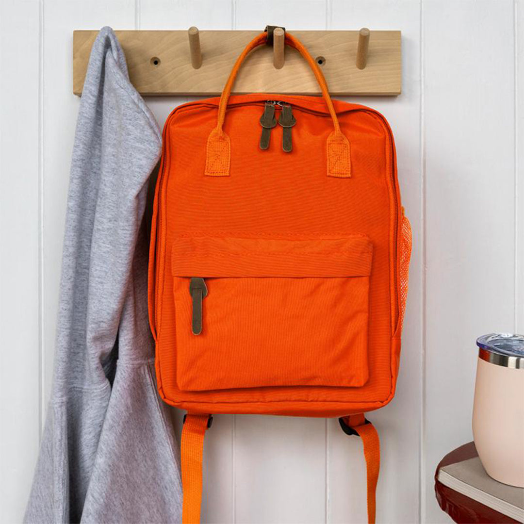 Oranje kinderrugzak hangt aan een houten kapstok naast een grijze trui.
