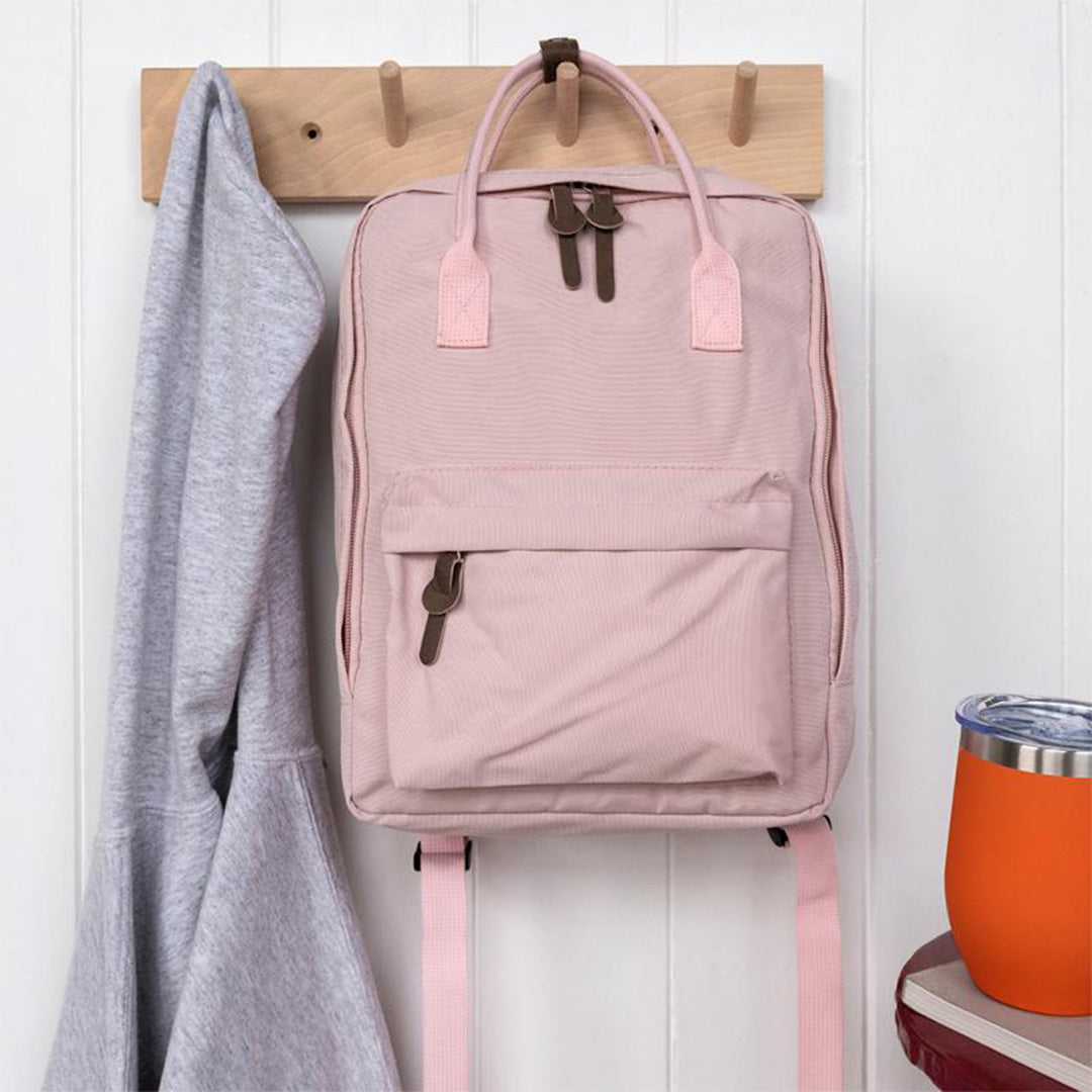 Roze Rex London kinderrugzak hangt aan een houten kapstok naast een grijze trui.