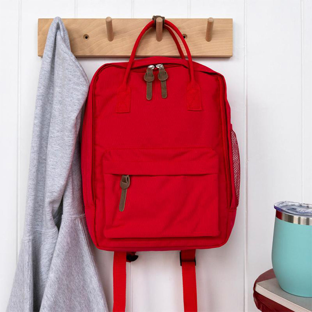 Rex London rode kinderrugzak hangt aan een houten kapstok naast een grijze trui.