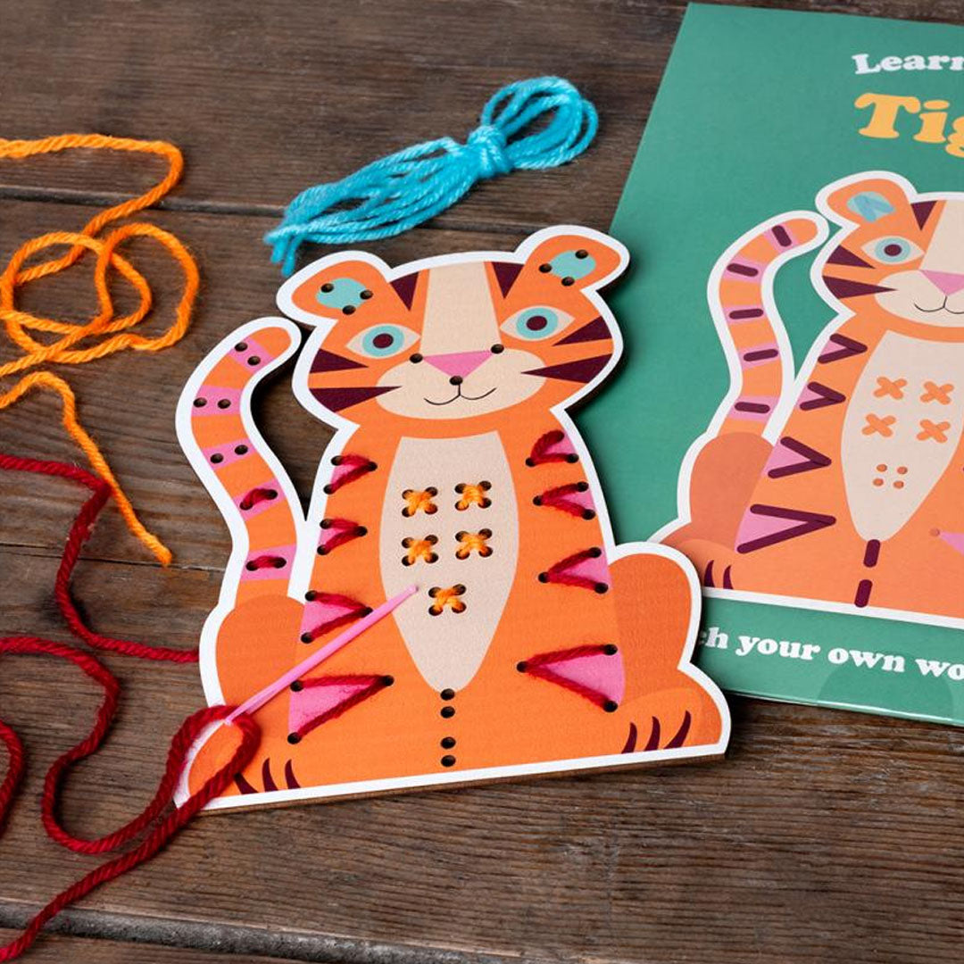 Een houten tijger rijgkaart met rode draad en een roze naald, liggend op een houten ondergrond.