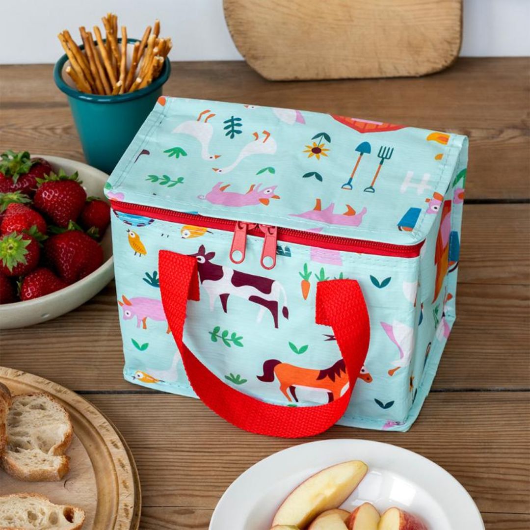 Kinderlunchtas met boerderijprint op een houten tafel met fruit en snacks.