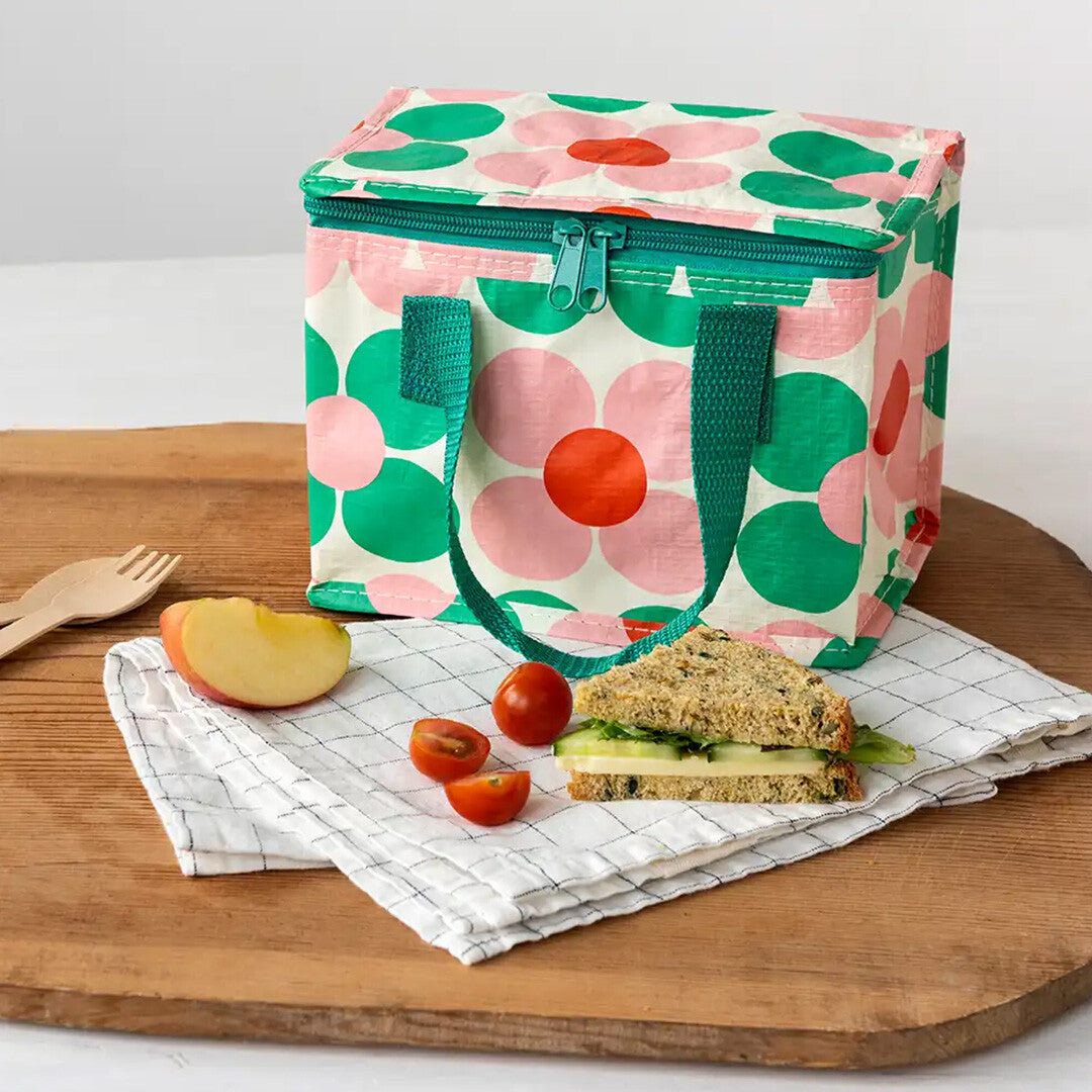 Rex London kinder lunchtas met bloemenpatroon op een houten plank met een broodje, appel en tomaatjes.