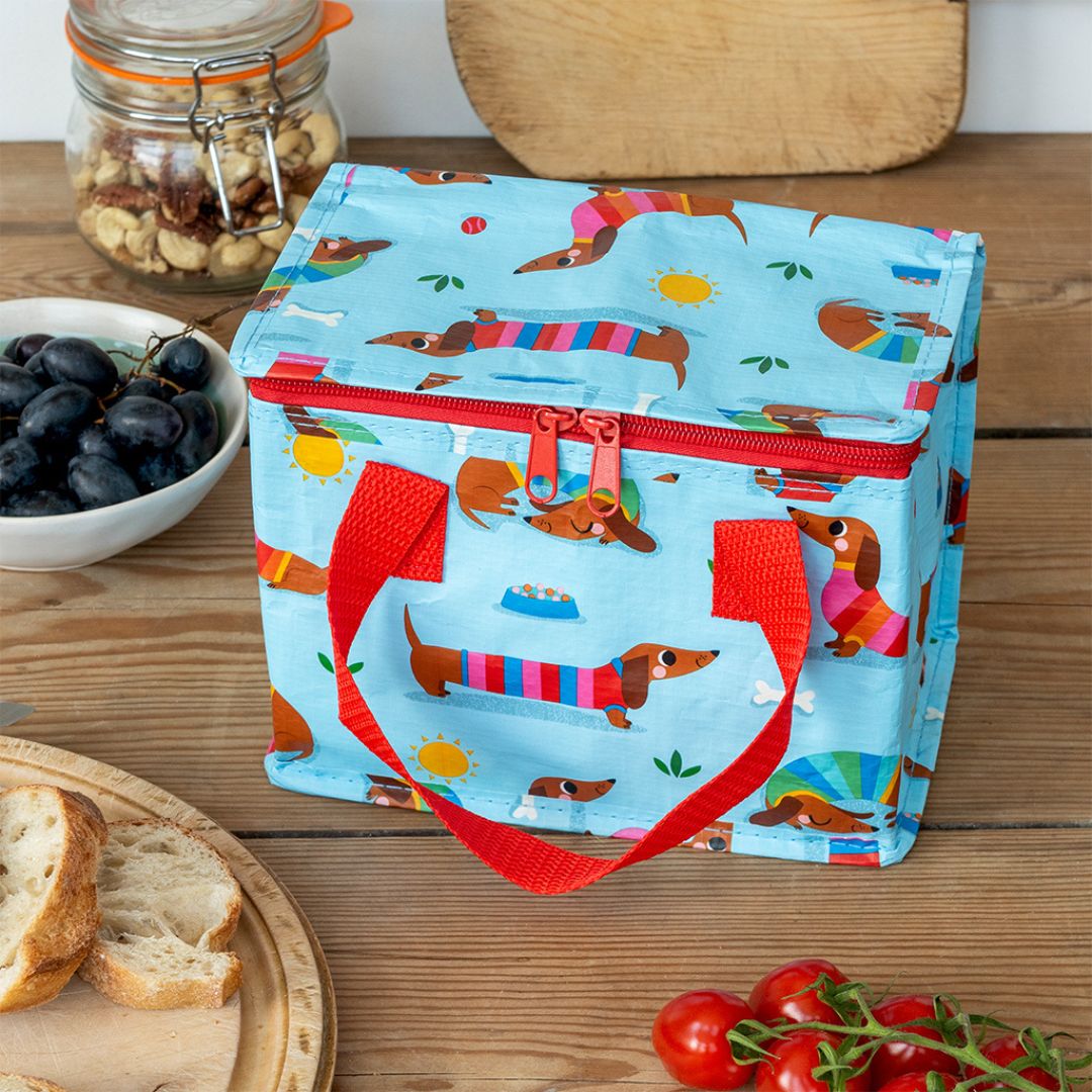 Rex London blauwe kinderlunchtas met worsthondjes op een houten tafel met eten.