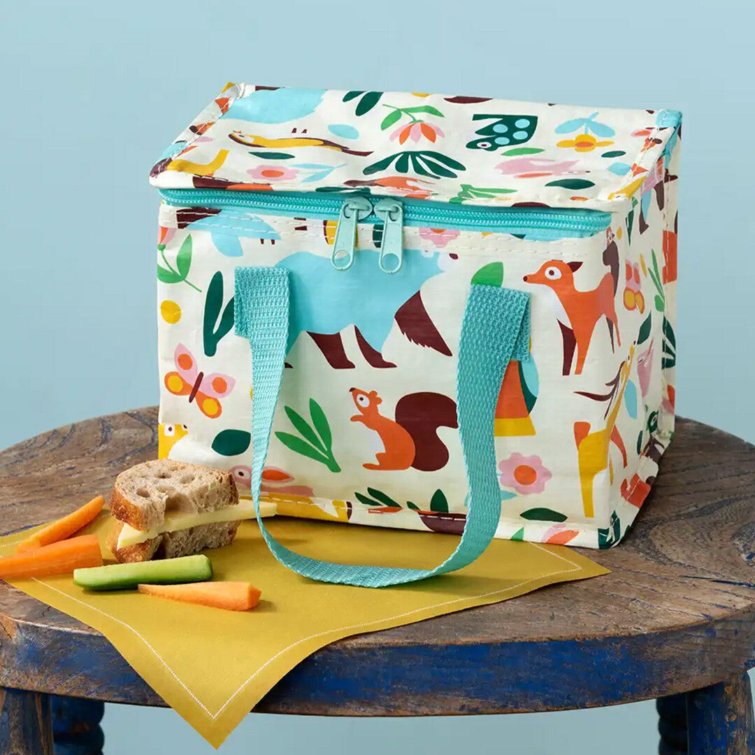 Rex London lunchtas met woodland dieren- en bloemenpatroon op een houten tafel met een broodje en groenten.