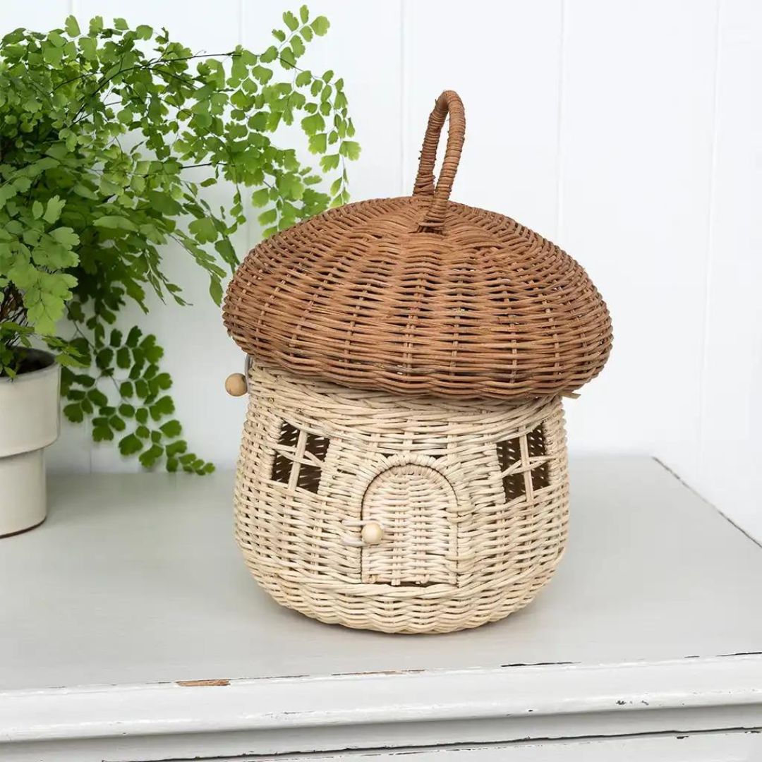 Rex London rotan paddenstoelhuis mand op een witte kast naast een plant.