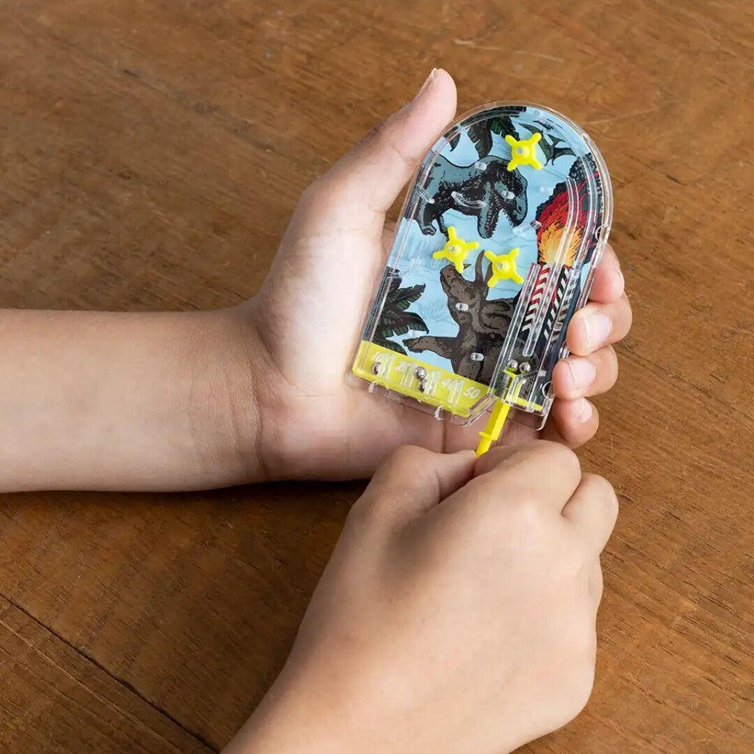 Kinderhanden die spelen met de Rex London mini flipperkast met prehistorisch land thema.
