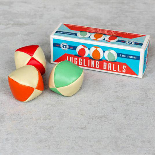 Drie Rex London jongleerballen in rood, oranje en groen met crèmekleurige vlakken, naast de verpakking op een grijze ondergrond.