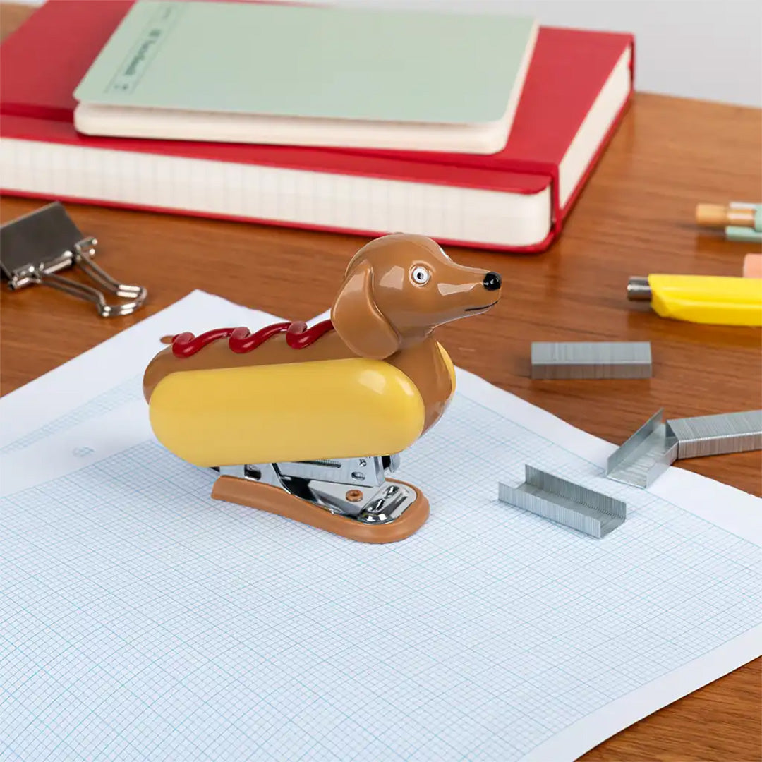 Rex London mini nietmachine in de vorm van een hotdog op een bureau met kantoorartikelen.
