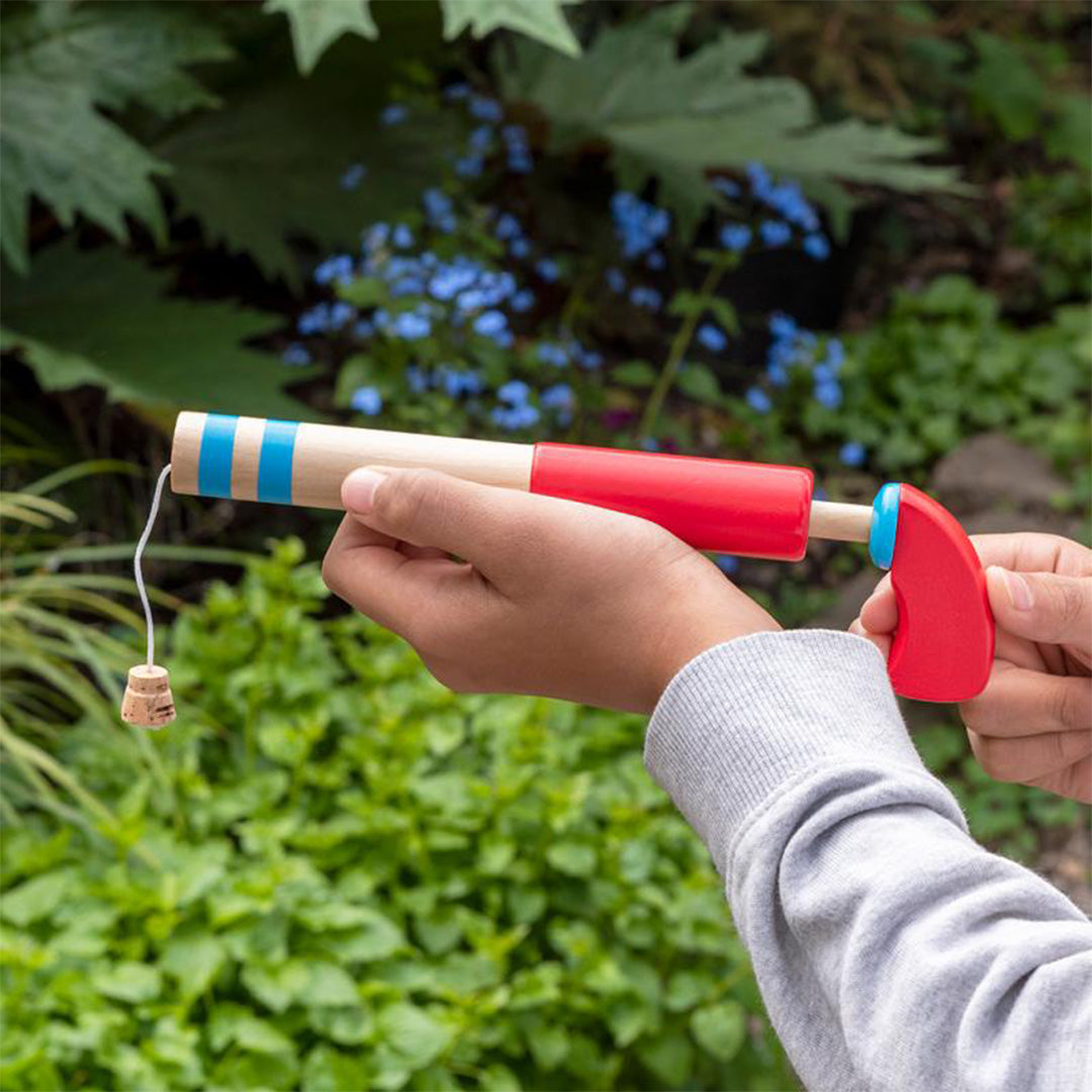 Een kind houdt de Rex London houten pop-gun met kurk vast in een tuin.