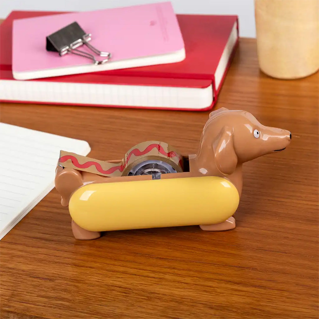 Rex London hotdog plakbandhouder op een houten bureau met plakband erin.