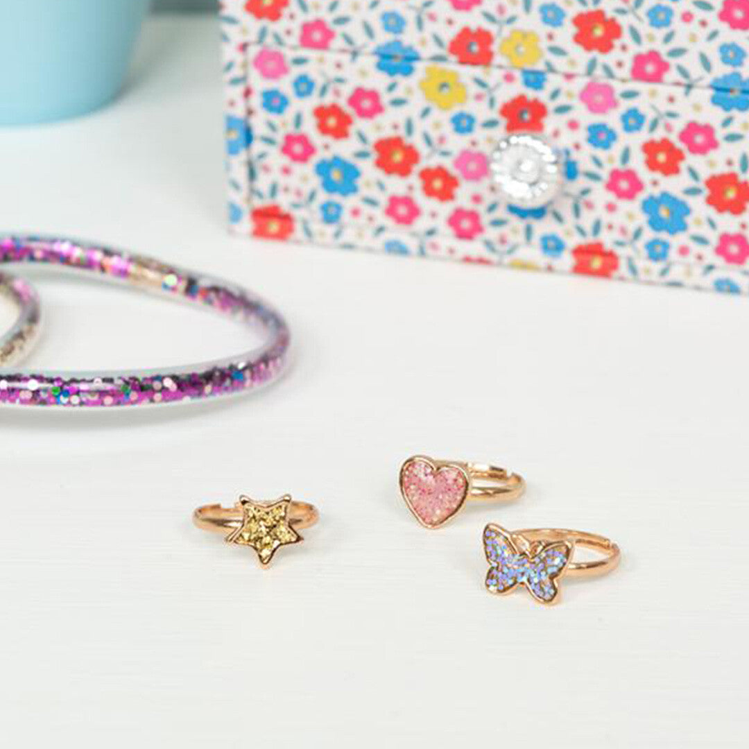 Drie Rex London Fairies in the Garden kinderringen, een glitter hart, een glitter vlinder en een glitter ster, liggen op een witte ondergrond.