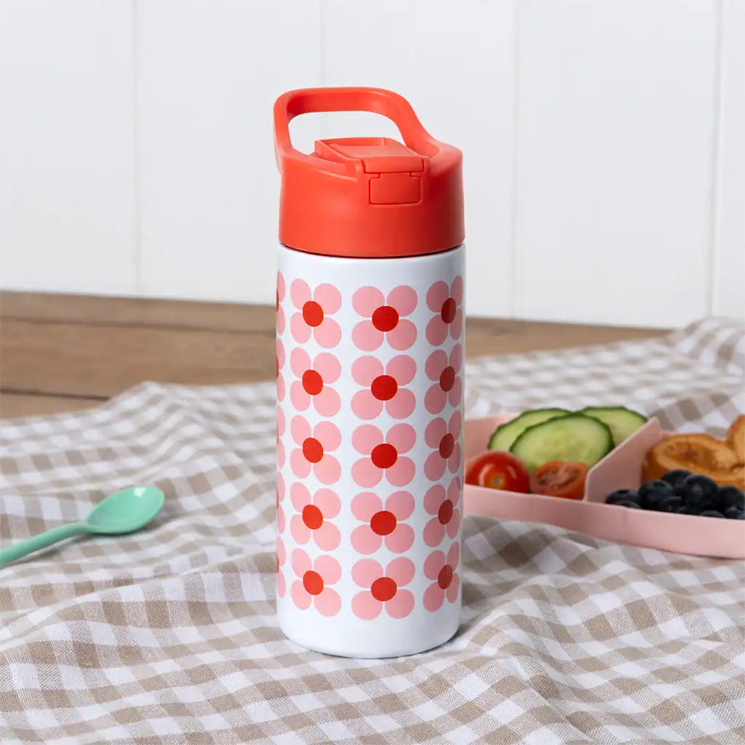 Rex London RVS drinkfles met roze madeliefjespatroon op een geruite picknickkleed naast een snackbox.