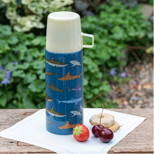 Rex London RVS thermosfles met haaienpatroon op een houten tafel met fruit en koekjes.