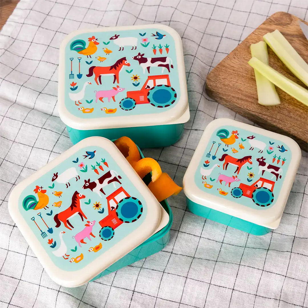 Drie Rex London snackdoosjes met boerderijthema op een geruite doek, waarvan één open met fruit.