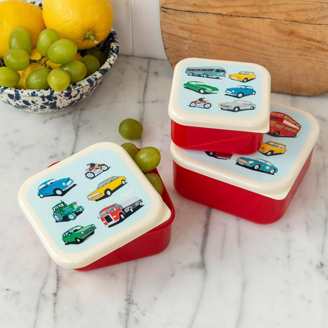 Twee rode Rex London snackdoosjes met voertuigprint op een aanrecht, één gevuld met druiven.