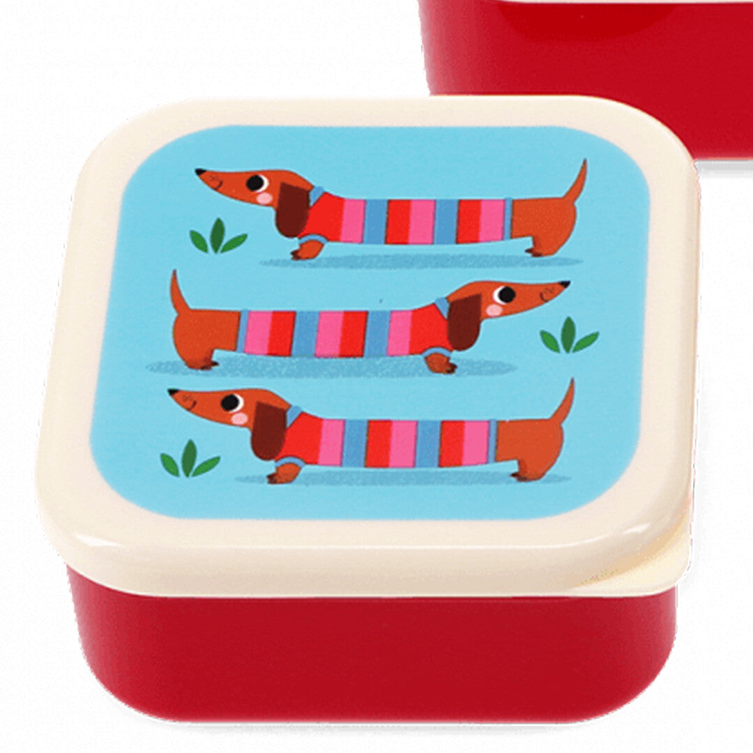 Detail van een rood snackdoosje met een deksel waarop drie teckels staan afgebeeld.