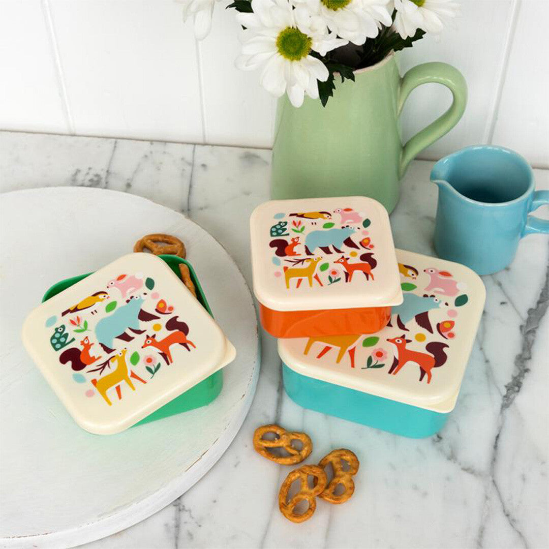 Drie rex london snackdoosjes met woodland dierenprint op een marmeren aanrecht, waarvan één open met pretzels, naast een vaas met bloemen.