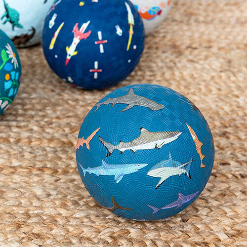Rex London blauwe speelbal met haaienprints op een rieten ondergrond, met andere speelballen op de achtergrond.