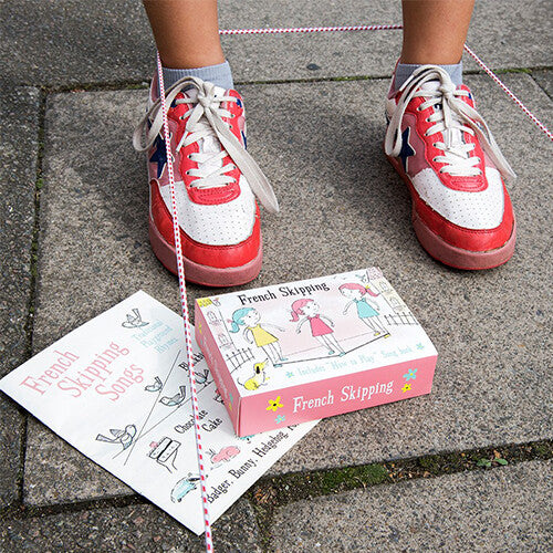 Voeten in rode sneakers demonstreren het Rex London springelastiek met het instructieboekje en de doos ernaast.