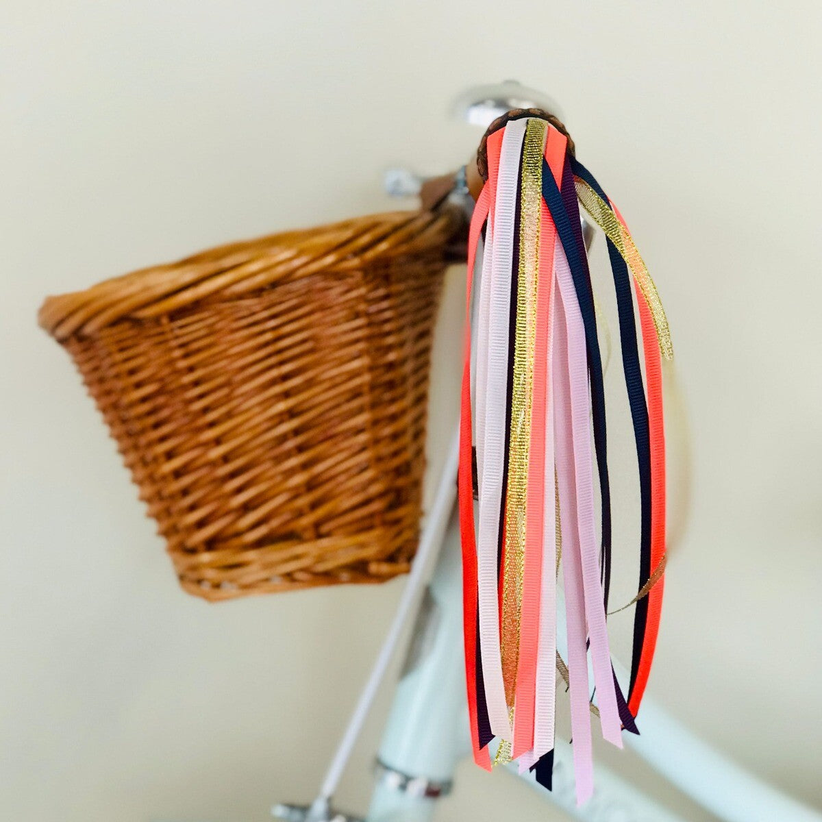 Detail van de veelkleurige Rex London stuurslingers aan het stuur van een fiets, naast een rieten mand.