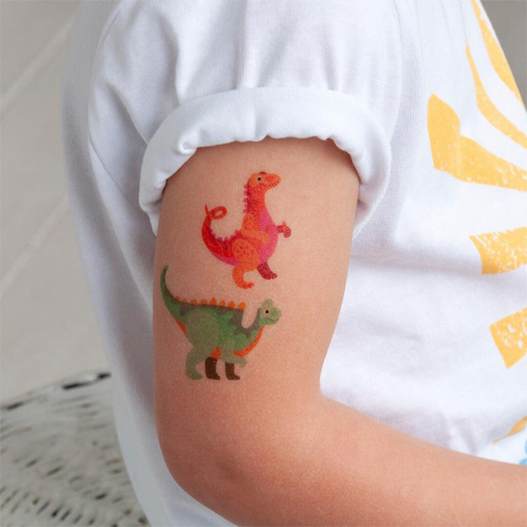 Arm van een kind met twee aangebrachte tijdelijke dinosaurus tatoeages, een rode en een groene.