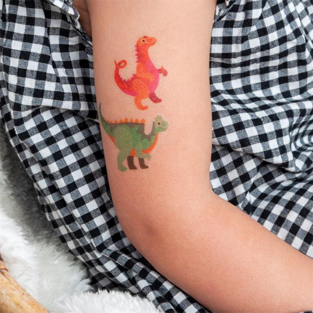 Arm van een kind met twee tijdelijke dinosaurus tatoeages, een rode en een groene, tegen een geruite achtergrond.