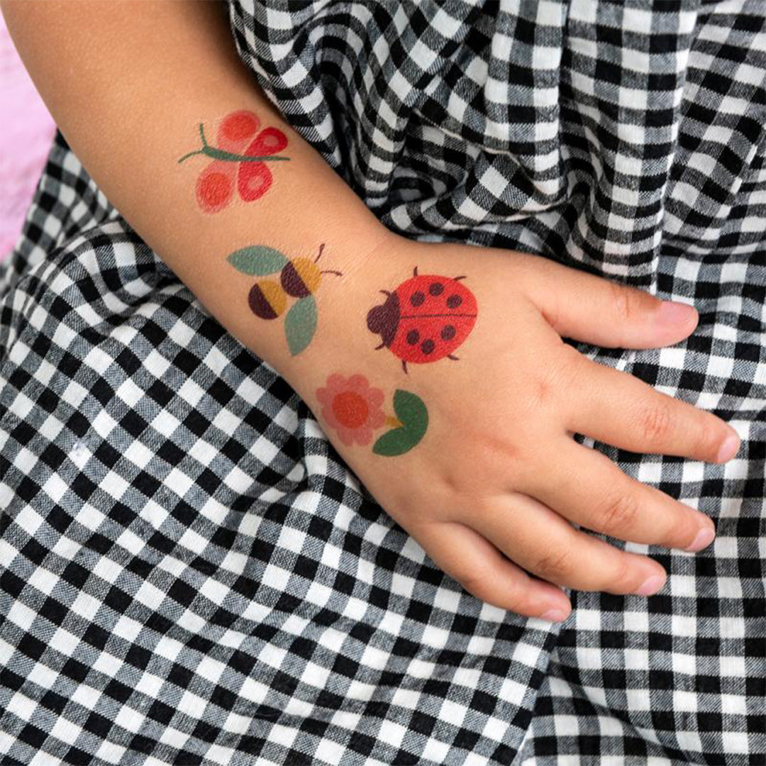Kinderarm met aangebrachte tijdelijke tatoeages van een vlinder, bij, lieveheersbeestje en bloem.