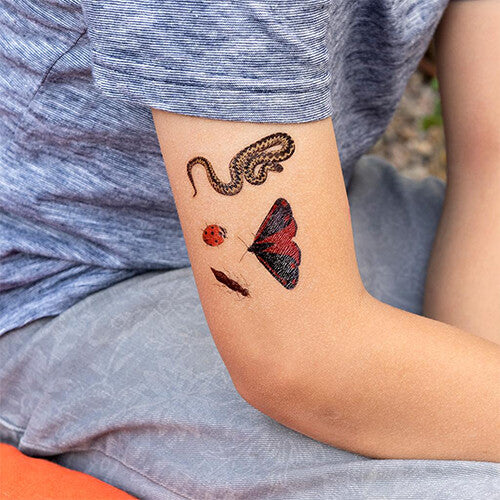 Een kinderarm met daarop aangebrachte tijdelijke tatoeages van een slang, lieveheersbeestje en vlinder met natuurthema.