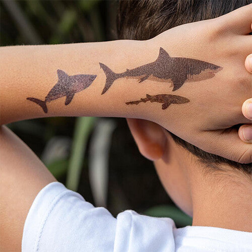 Een kinderarm met drie tijdelijke haaien tattoos.