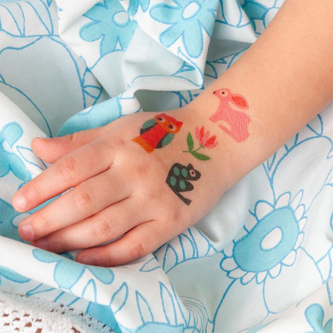 Drie tijdelijke tatoeages van een uil, konijn en kikker met een bloem op de hand van een kind.