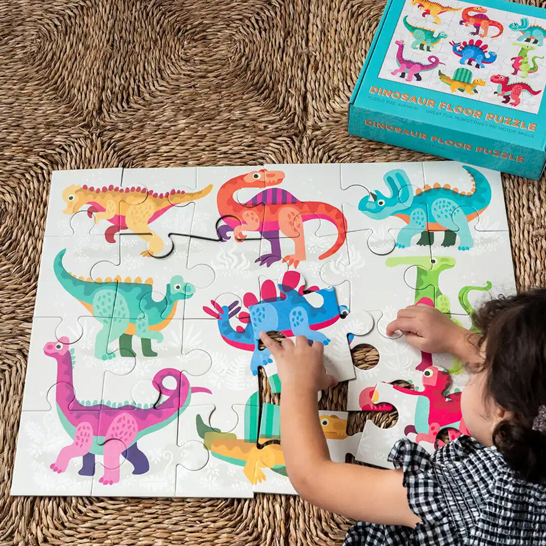 Een kind legt een stukje van de Rex London vloerpuzzel met dinosaurussen op een gevlochten mat.