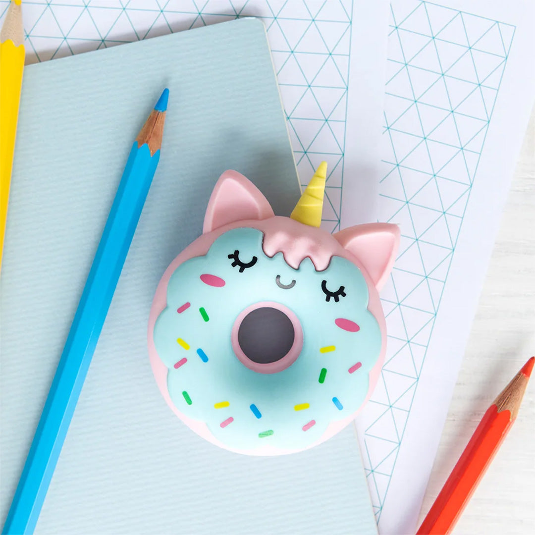 Rex London eenhoorn donut gum op een blauw notitieboekje, omringd door kleurpotloden.