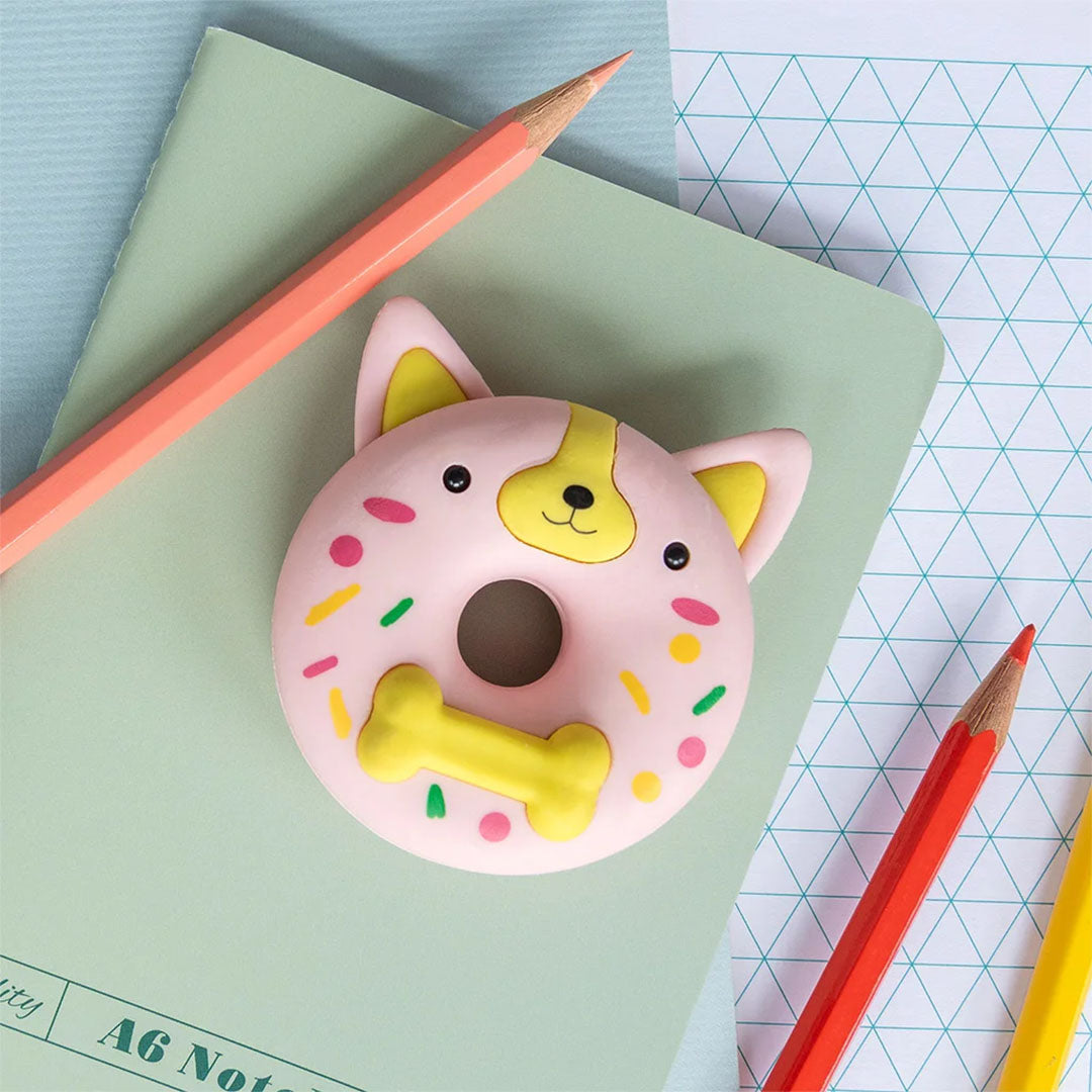De roze donutvormige gum met hondenhoofd ligt op een groen notitieboekje naast kleurpotloden.