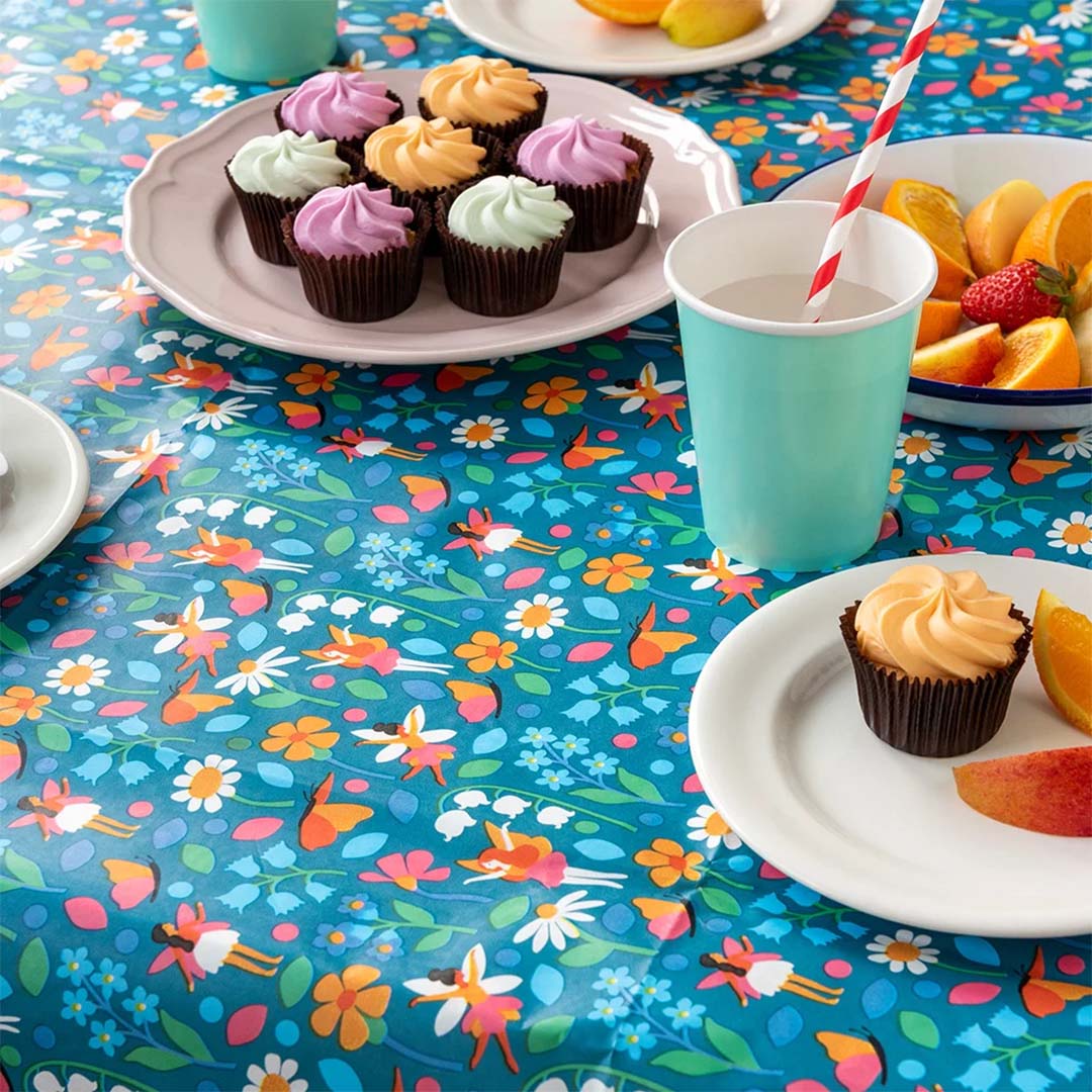 Gedekte tafel met het papieren tafelkleed met feeën en bloemenpatroon, cupcakes en fruit.