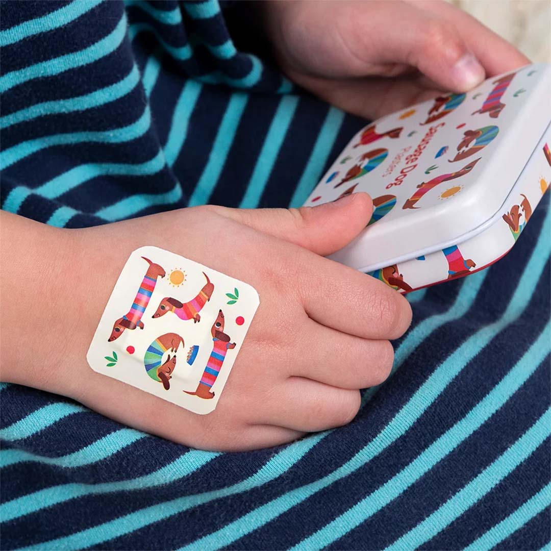 Een Rex London worstjeshond pleister op de hand van een kind, met het bijpassende blikje op de achtergrond.