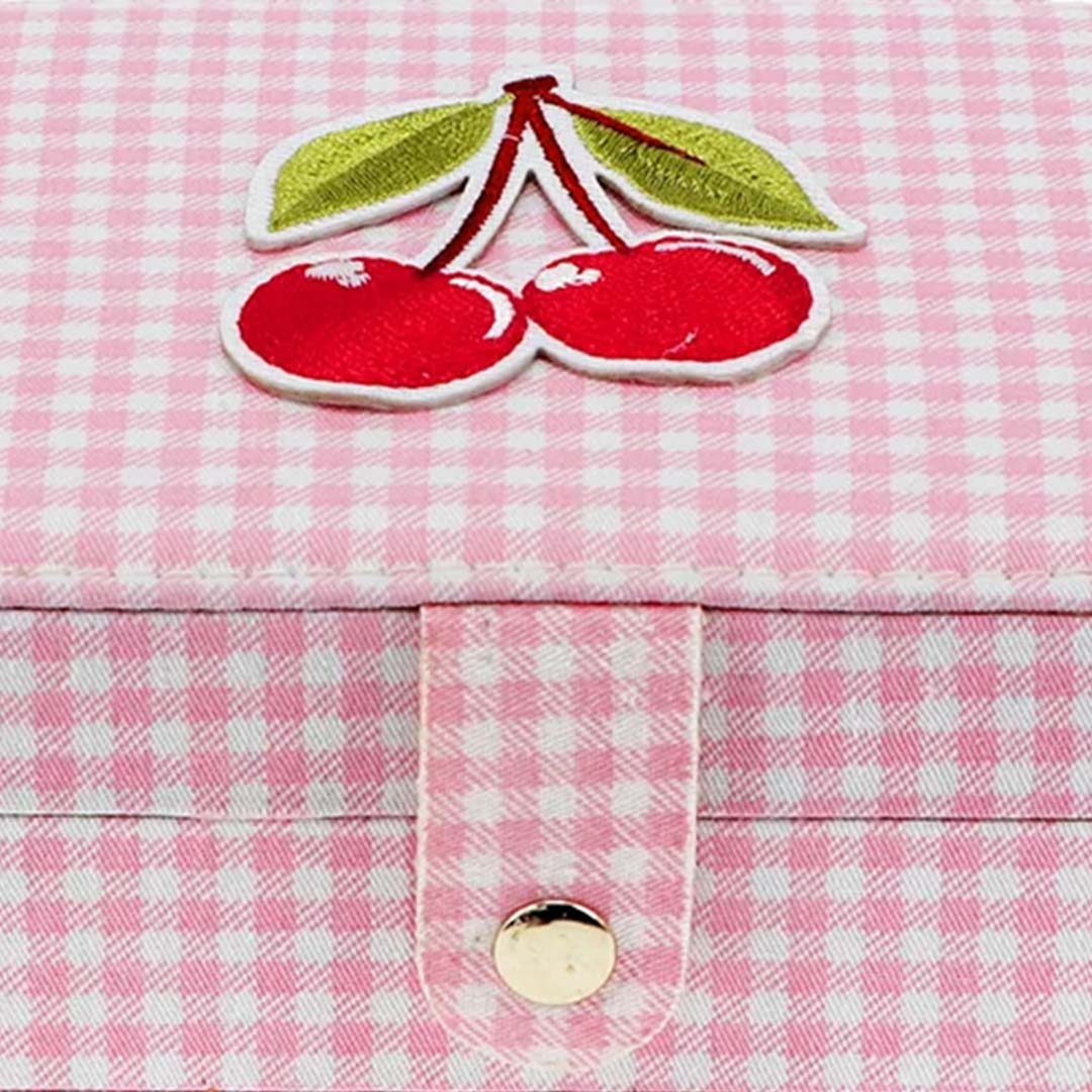 Detail van het Rex London sieradendoosje met roze ruitpatroon, de geborduurde kersen en de gouden drukknoopsluiting.