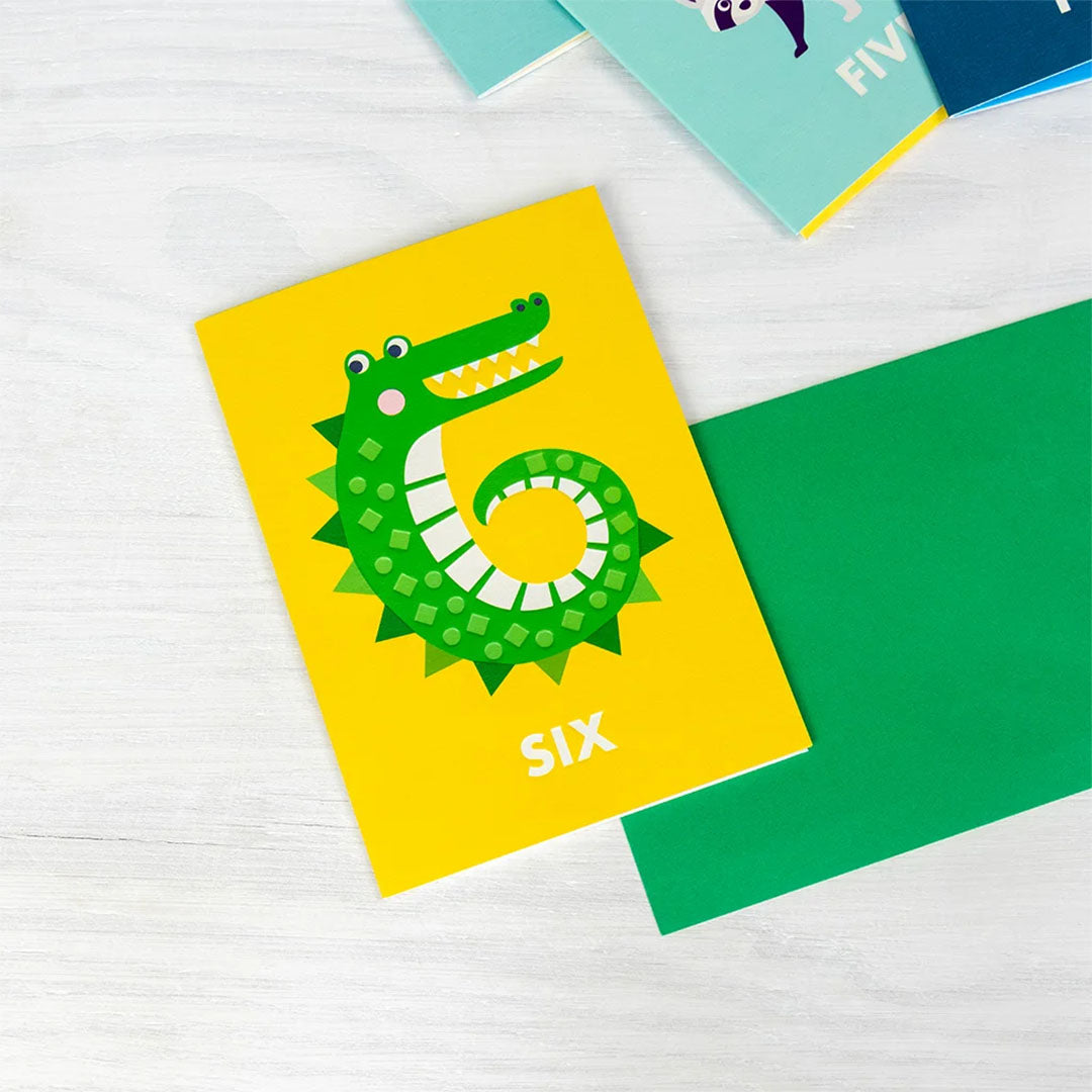 Rex London verjaardagskaart met een groene krokodil en het cijfer 6, liggend op een witte houten ondergrond.