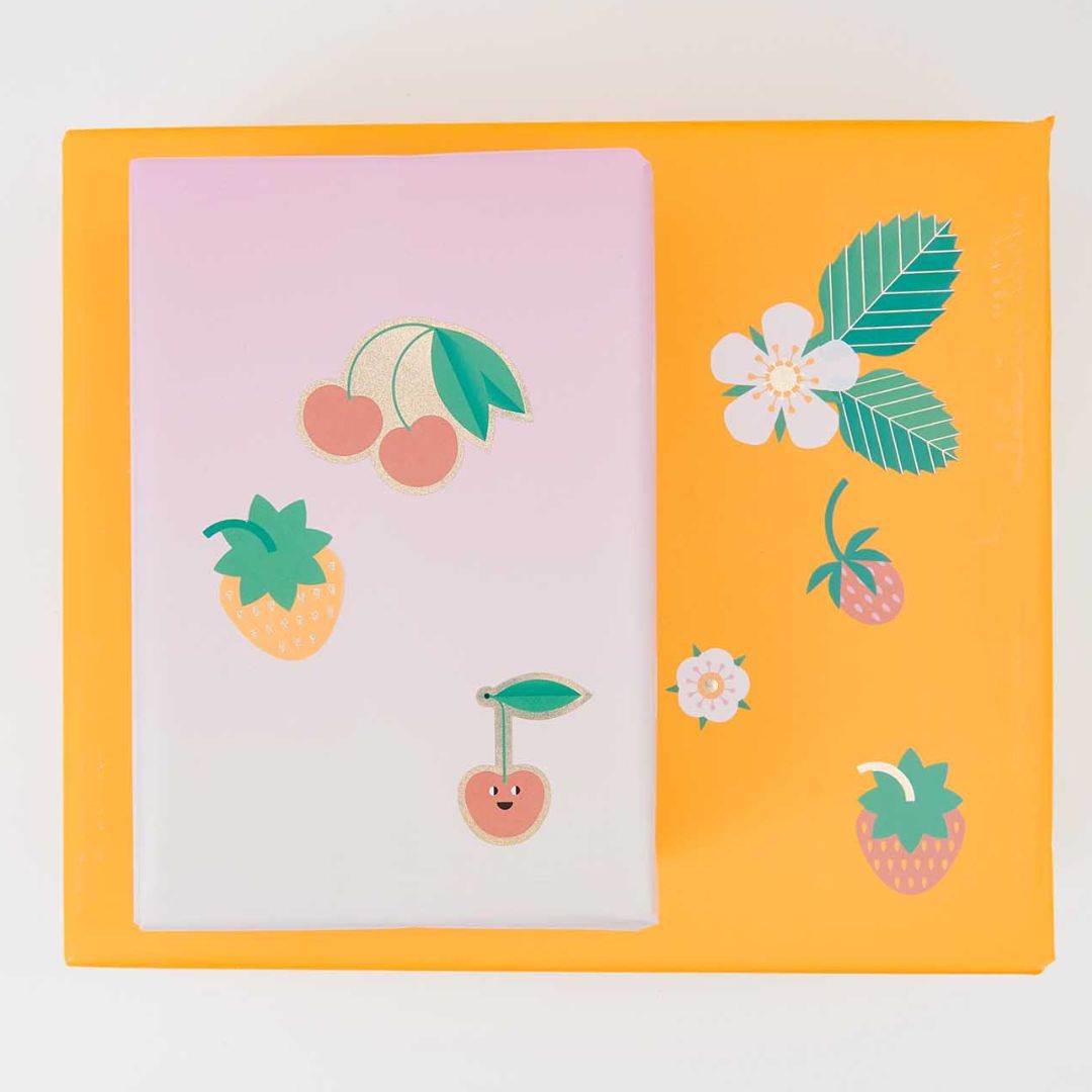 Fruit- en bloemstickers geplakt op een roze notitieboek en een gele doos.
