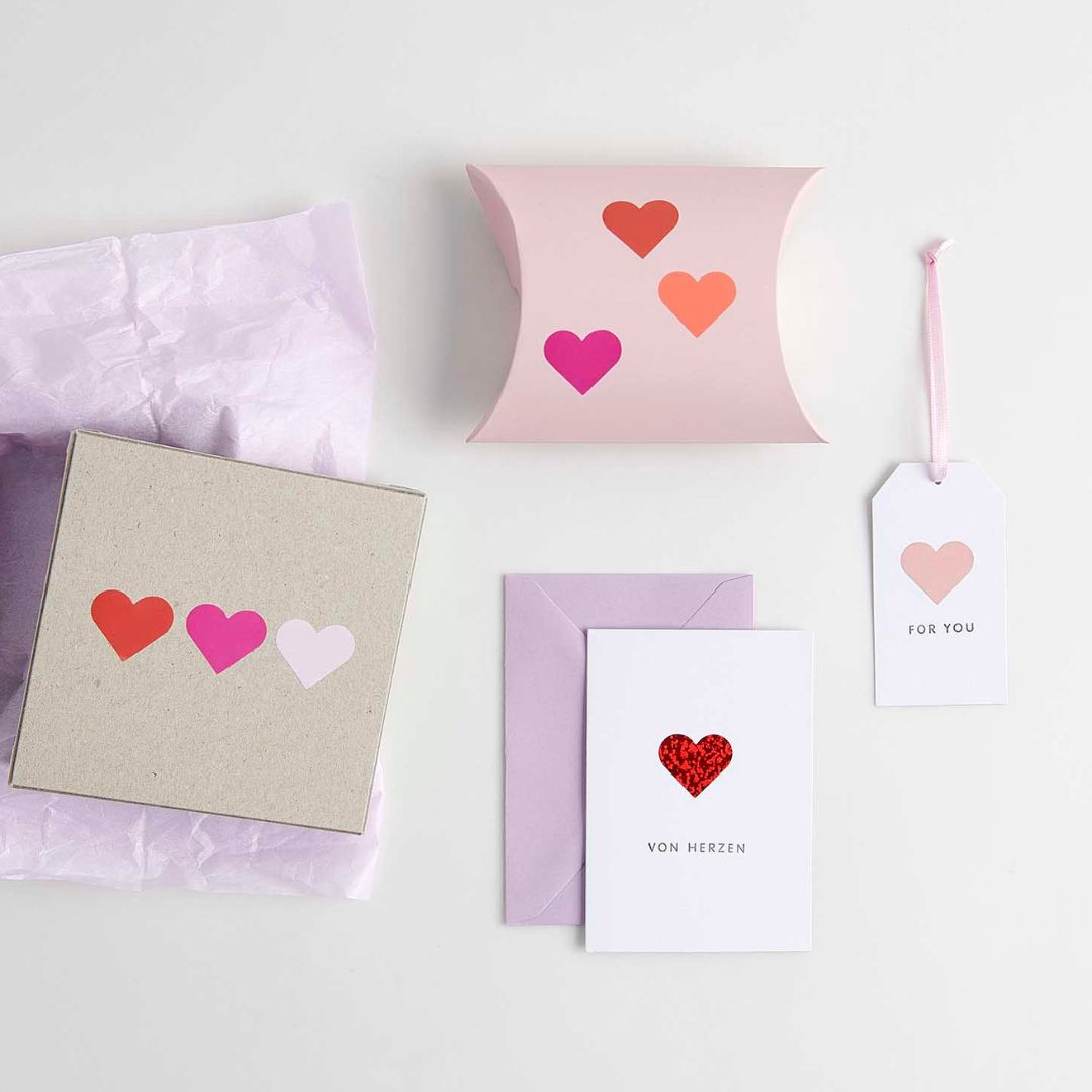 Diverse knutselitems versierd met Rico Design hartstickers in verschillende kleuren, waaronder een cadeaubox en een kaartje.