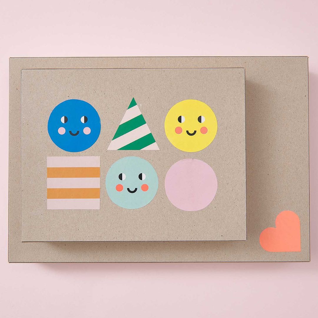 Decoratieve stickers met geometrische vormen en gezichtjes, waaronder een blauwe cirkel en een groen gestreepte driehoek, op een kartonnen ondergrond.