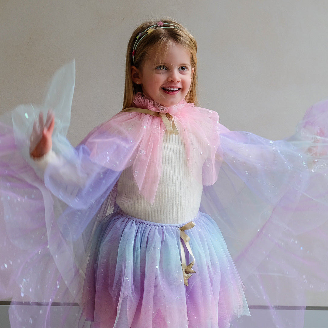 Lachend meisje draagt een mimi & lula pastelkleurige verkleedrok en bijpassende cape met glittersterren.