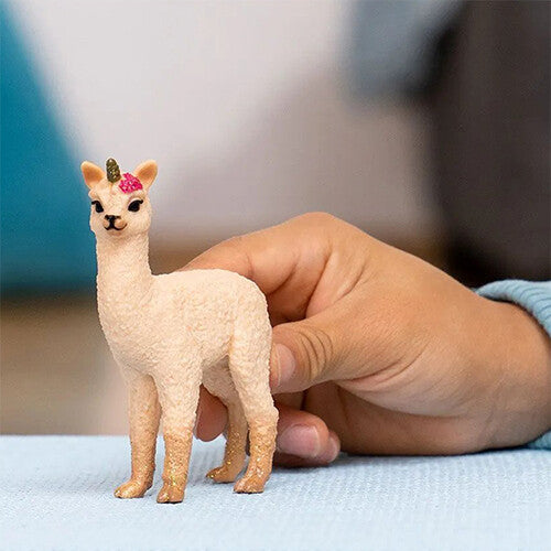 Een kinderhand houdt het Schleich lama-eenhoorn veulen speelgoedfiguur vast, wat de grootte van het figuur toont.