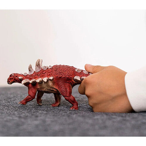 Het rode Gastonia dinosaurusspeelfiguur op een donkere ondergrond, met een hand die de schaal toont.